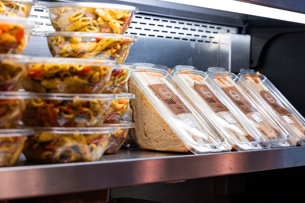 Delicious ready-to-eat pasta salads and sandwiches displayed in a store fridge.