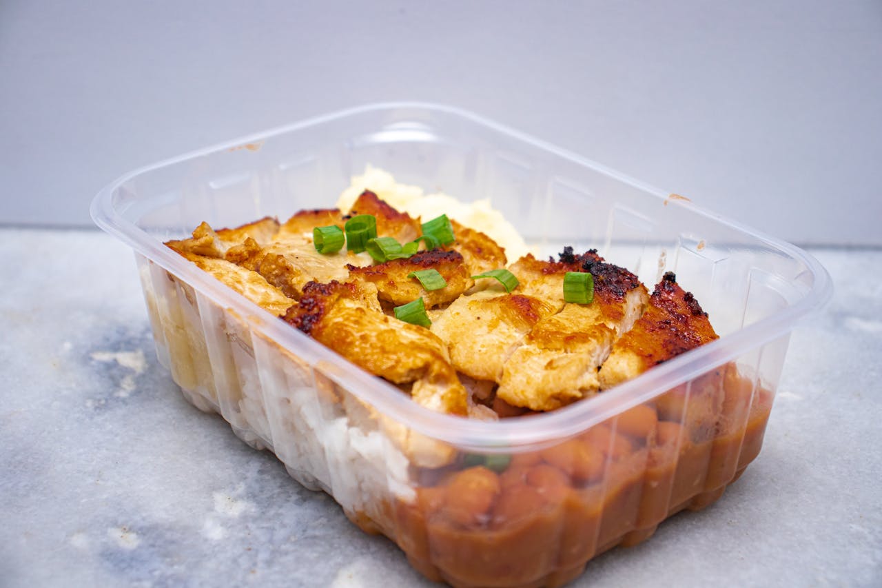 Delicious grilled chicken with beans and rice in a clear takeout container.