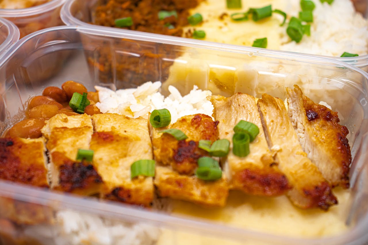 Close-up of a grilled chicken meal in a plastic container, garnished with green onions.